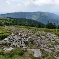 Kamienny szlak i kopczyk na górskim szczycie. W oddali widać zalesione pasma górskie, idealne miejsce na odkrywanie międzylesie atrakcje.