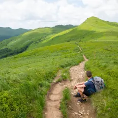 Turysta odpoczywa na szlaku, podziwiając zielone połoniny. Bieszczady atrakcje czekają!