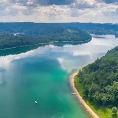 Malownicze jezioro otoczone lasami, z łodziami przy brzegu. Idealne miejsce na wypoczynek i odkrywanie atrakcji w Polsce.