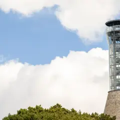 Nowoczesna wieża widokowa na Śnieżniku, otoczona zielenią drzew i błękitem nieba z białymi chmurami.
