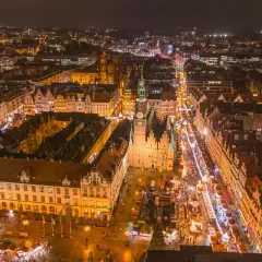 Nocny widok na Wrocławski Rynek, gdzie tętni życiem największy jarmark bożonarodzeniowy w Polsce. Kolorowe iluminacje i tłumy ludzi tworzą magiczną atmosferę.