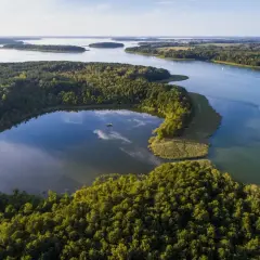 Malownicze jeziora i lasy, idealne miejsca na wakacje. Widać łódkę na spokojnej wodzie i żaglówki na większym akwenie.
