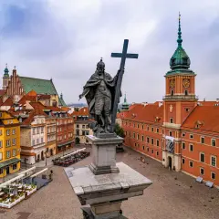 Pomnik króla Zygmunta III Wazy na placu Zamkowym, w tle Zamek Królewski i kolorowe kamienice Starego Miasta. Dwie wieże Warszawy w oddali.