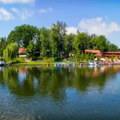 Malowniczy widok na port i jezioro w Rucianem Nidzie. Widać tu liczne łodzie, restauracje i zielone drzewa, tworzące idealne miejsce na wypoczynek i odkrywanie atrakcji.