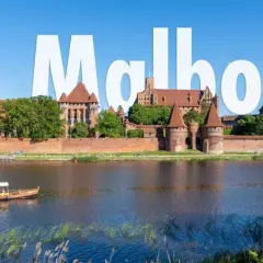 Malbork atrakcje: potężny zamek krzyżacki nad rzeką, z łodzią turystyczną na pierwszym planie.