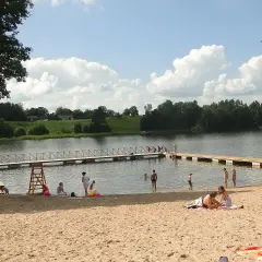 Słoneczne plaże na Mazurach tętnią życiem. Ludzie odpoczywają na piasku, kąpią się w jeziorze i spacerują po pomoście.