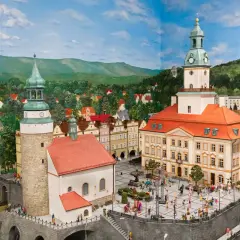 Miniaturowa panorama miasta z wieżami i placem pełnym ludzi. W tle góry i lasy, idealne na odkrywanie atrakcji w okolicy Jeleniej Góry.
