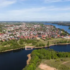 Widok z lotu ptaka na miasteczko nad jeziorem, jedno z największych rynków w Polsce, z domami z czerwonymi dachami i zielenią.