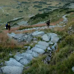 Dwóch turystów wędruje kamienistym szlakiem po zboczu górskim. Tatry atrakcje to wspaniałe widoki i wyzwania dla każdego miłośnika gór.