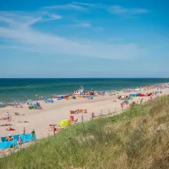 Słoneczna plaża w Dąbkach pełna turystów, kolorowych parawanów i łodzi. Idealne miejsce na wakacyjne atrakcje nad Bałtykiem.