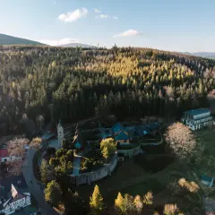 Kolorowy kompleks budynków, w tym hotel i kościółek, otoczony lasem. To idealne miejsce na **centrum rekreacji i sportu**, gdzie można odpocząć wśród natury.