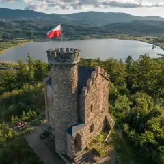 Kamienna wieża z polską flagą na szczycie, w tle jezioro i góry. Idealne miejsce, by odkryć, co warto zobaczyć w Sudetach.