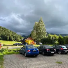 Samochody na parkingu pod Babią Górą, w tle las i chmury.