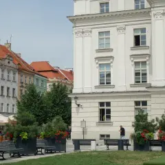 Kalisz atrakcje: biały budynek z kolumnami, kamienice z czerwonymi dachami, ławki i zielone donice z kwiatami.