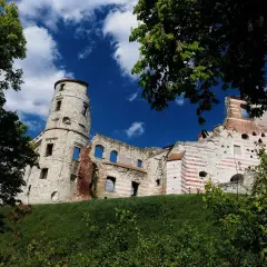 Zamek w Janowcu, ruiny zamku z charakterystyczną wieżą, na tle błękitnego nieba z chmurami.