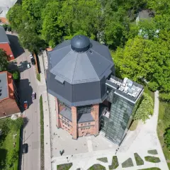 Nowoczesna wieża ciśnień w Zabrzu z przeszkloną windą i tarasem widokowym, otoczona zielenią.
