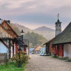 Sanok atrakcje: skansen z drewnianymi domami i wieżą, otoczony mglistymi wzgórzami.