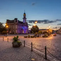 Wieczorny rynek w Nowym Sączu, oświetlony latarniami i iluminacją ratusza. Brukowana nawierzchnia i zabytkowa architektura tworzą niepowtarzalny klimat, zachęcając do odkrywania atrakcji Nowego Sącza.