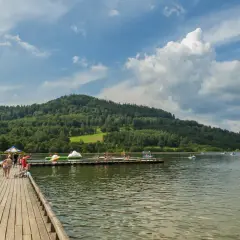 Ludzie odpoczywają nad zalewem Stara Morawa. Widać drewniane molo, wieżę ratowniczą, pływające atrakcje i łódki.