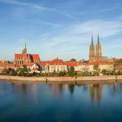 Widok na Ostrów Tumski, serce starego miasta Wrocławia, z katedrą i kościołem św. Krzyża odbijającymi się w spokojnej wodzie Odry.