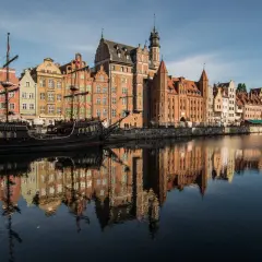 Gdańsk atrakcje: zabytkowy żaglowiec cumuje przy Motławie, w tle kolorowe kamienice i Żuraw. Odbicia budynków w wodzie.