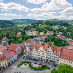 Urokliwy rynek i kolorowe kamienice w Dusznikach Zdroju. W tle zielone wzgórza, idealne na piesze wycieczki i odkrywanie atrakcji.
