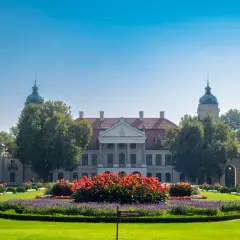 Pałac Zamoyskich w otoczeniu zieleni i kwitnących rabat. Majestatyczna budowla z kolumnowym portykiem i kopułami.