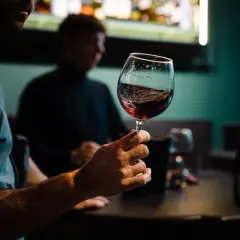 Degustacja wina w Warszawie. Mężczyzna trzyma kieliszek czerwonego wina, w tle inny uczestnik i butelki.