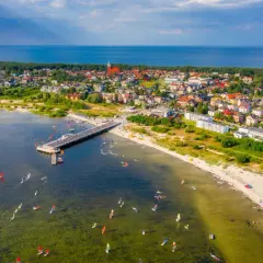 Jastarnia atrakcje: molo, plaża z turystami i liczne żaglówki oraz deski windsurfingowe na wodzie.