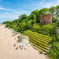 Piękna plaża z ruinami na klifie, zielone tarasy i ludzie odpoczywający na piasku. Trzęsacz atrakcje zachwycają!