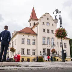 Mężczyzna podziwia ratusz w Trzebnicy, jedno z głównych atrakcji miasta. W tle zabytkowy budynek z zegarem i czerwonym dachem.