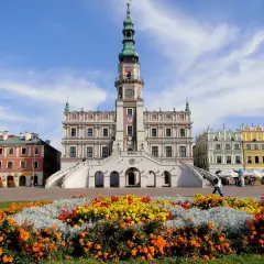 Zamość atrakcje: Ratusz i kolorowe kamienice na Rynku Wielkim, otoczone kwitnącymi rabatami.