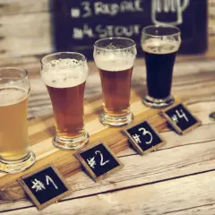Degustacja piwa w Poznaniu: cztery szklanki z różnymi piwami, oznaczone numerami od 1 do 4, na drewnianej desce.