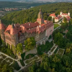 Zamek Książ otoczony lasami, z malowniczymi ogrodami i pobliską wsią. Rudawy Janowickie w tle.