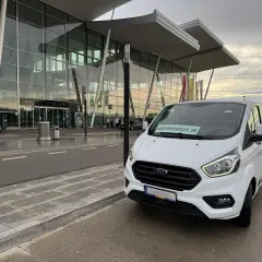 Biały bus przed nowoczesnym terminalem lotniska. Szukasz taniego parkingu lotnisko Wrocław?