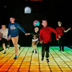 Dzieci biegają po interaktywnej podłodze PXL w Krakowie, rozświetlonej kolorowymi pikselami.