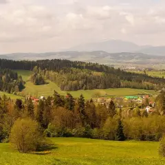 Malowniczy krajobraz z lasami i polami, w oddali widać góry i zabudowania. To idealne miejsce na odkrywanie rabka-zdrój atrakcje.