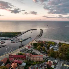 Widok na port i plażę w Ustce. Widać łodzie, latarnię morską i zabudowania. To jedne z wielu ustka atrakcje.