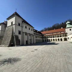 Zamek w Suchej Beskidzkiej, z dziedzińcem wyłożonym kamienną kostką i arkadowymi krużgankami, prezentuje się majestatycznie pod błękitnym niebem.