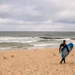 Surfer z deską na plaży w Juracie, szuka fal. W tle morze i mewy. Jedna z atrakcji nad polskim morzem.