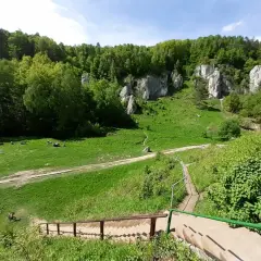Malownicza Dolina Kobylańska z zielonymi łąkami, skalnymi ostańcami i lasem. Ludzie odpoczywają, a rowery czekają na wycieczkę.