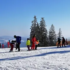 Słoneczny stok narciarski w Bieszczadach, z grupą narciarzy i snowboardzistów, w tym dzieci, przygotowujących się do zjazdu.