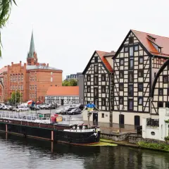 Bydgoszcz atrakcje: nad Brdą, w tle zabytkowe kamienice i kościół. Na pierwszym planie barka i rzeźba.