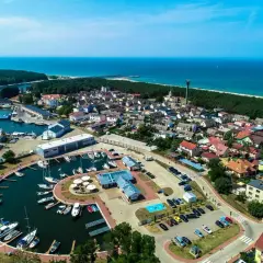 Widok z lotu ptaka na Dziwnów: port jachtowy, domy, las i morze. Wiele łodzi zacumowanych w marinie, idealne miejsce na wakacje.