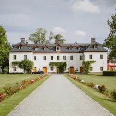 Malowniczy pałac otoczony zielenią, z alejką prowadzącą do wejścia. To miejsce, gdzie można poczuć atmosferę doliny pałaców i ogrodów.