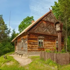 Drewniane chaty i kapliczka na słupie w jednym z polskich skansenów. Wiosenna zieleń otacza zabytkowe budynki.