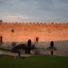 Zamek w Szydłowie o zachodzie słońca. Ludzie odpoczywają na trawie, podziwiając historyczne atrakcje.