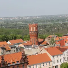 Widok na Chełmno z charakterystyczną wieżą ciśnień. Miasto z czerwonymi dachami i zielenią w tle. Chełmno atrakcje warte zobaczenia.