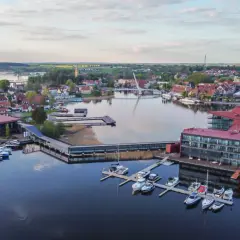 Malownicze mazury miejscowości z nowoczesną architekturą nad jeziorem, pełne łodzi i jachtów.