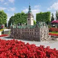 Miniatura ratusza z wieżą i zegarem, otoczona czerwonymi kwiatami. Jedna z wielu kłodzko atrakcje.